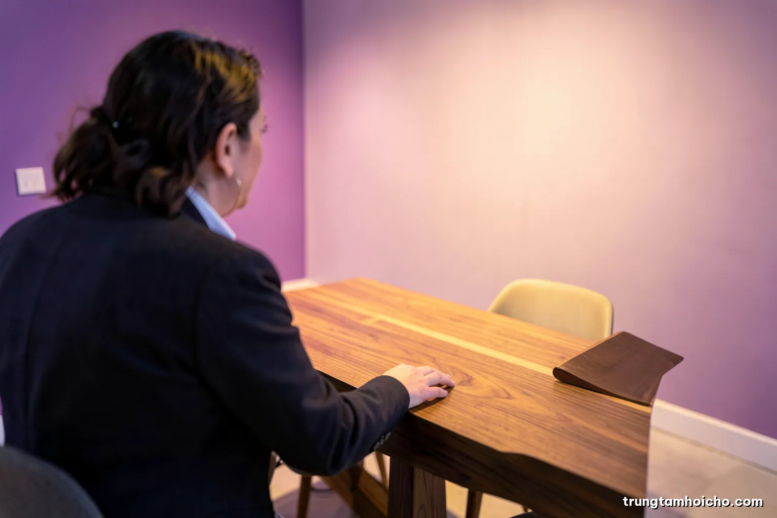 Over-the-shoulder view of a buyer touching the grain of a solid wood dining table in a minimalist showroom booth, soft diffused light, walnut brown and cream palette, interior design magazine style