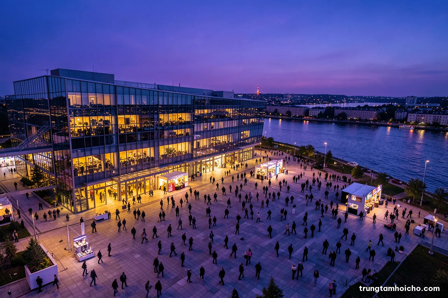 Wide aerial view of a modern convention centre beside a river at dusk, guests walking across a plaza, warm interior glow, deep blue and amber palette, editorial magazine photography