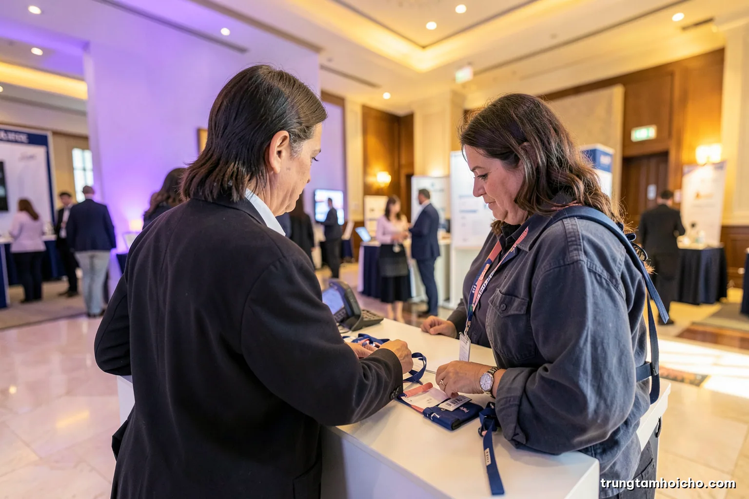 Over-the-shoulder view of an organiser arranging blank lanyards and headsets on a registration desk in a spacious hotel foyer, soft morning light, ivory and slate blue palette