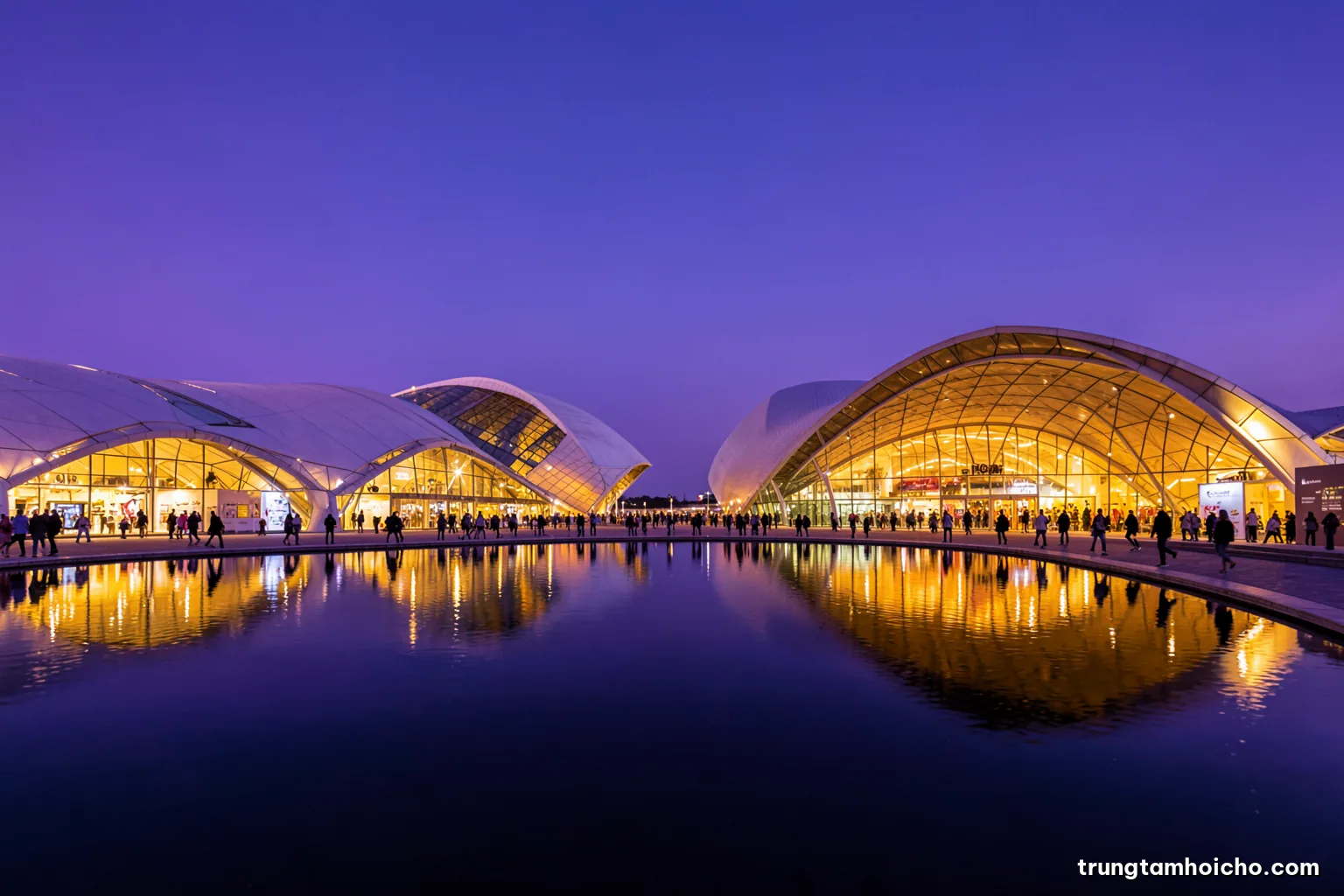 Wide dusk view of futuristic national pavilions with sweeping curved architecture reflected in a calm pool, crowds as tiny silhouettes, indigo sky and warm architectural lighting, editorial travel photography