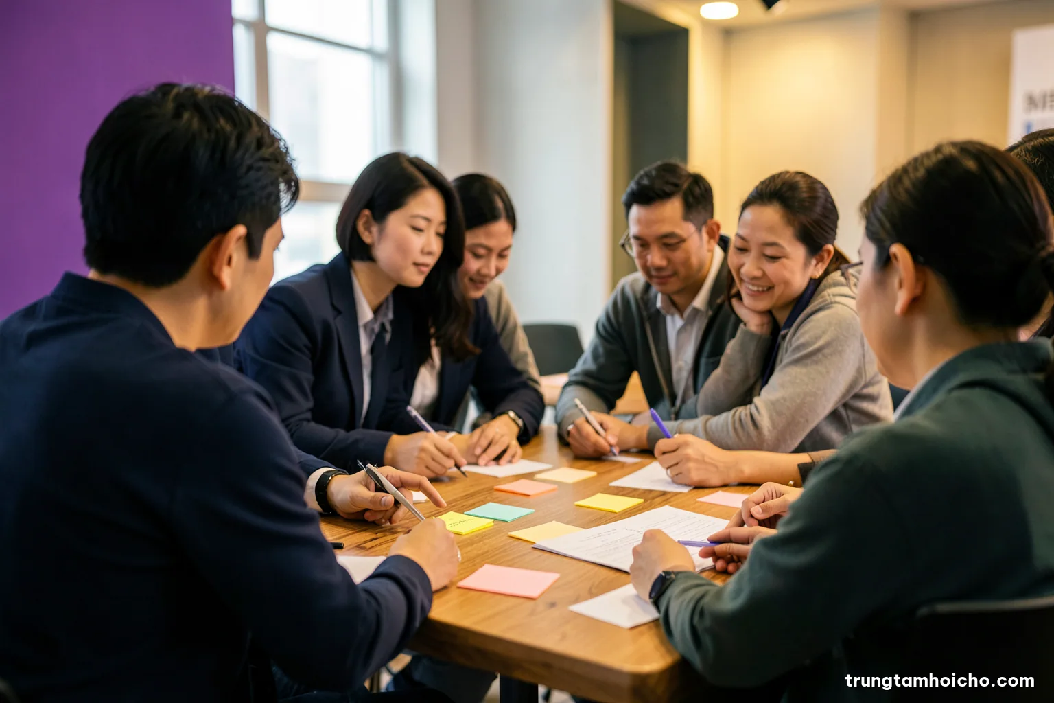 Over-the-shoulder view of a Vietnamese marketing team planning around a long wooden table with sticky notes and blank cards, soft morning window light, muted teal and sand tones
